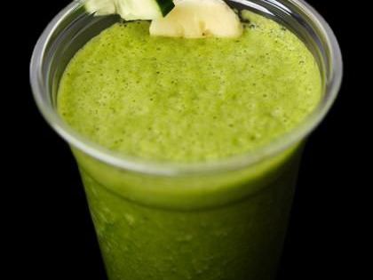 A cup of vivid green smoothie garnished with a slice of cucumber and a piece of ginger.