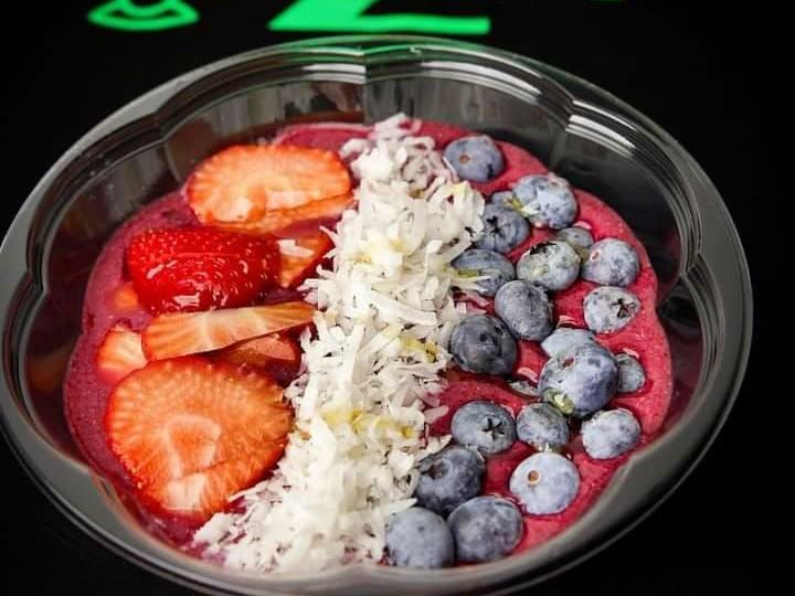 A deep pink smoothie bowl topped with sliced strawberries, a stripe of coconut flakes and blueberries.