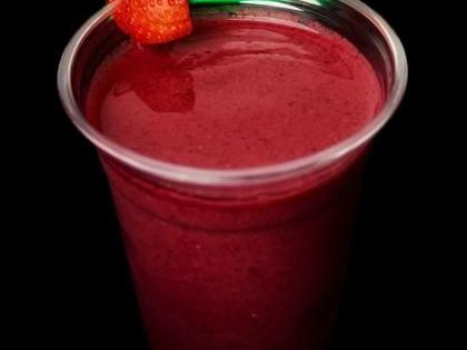 A cup of deep red berry smoothie with a strawberry on the rim.