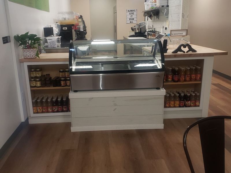 The Tazza service counter with a glass display case, shelves of bottled drinks either side and a green feature wall.