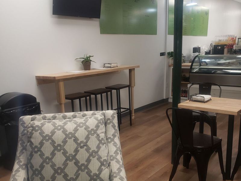 The far end of the room: a wall-mounted screen, a green panel, a bar-height counter with stools and café tables.