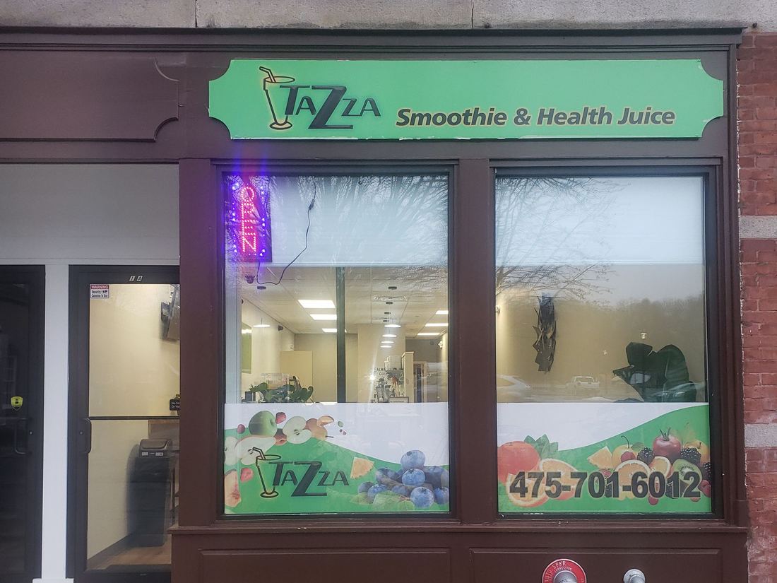 The Tazza shopfront on Church Street: a green sign reading Tazza Smoothie & Health Juice above a dark red timber window, with a neon OPEN sign inside.